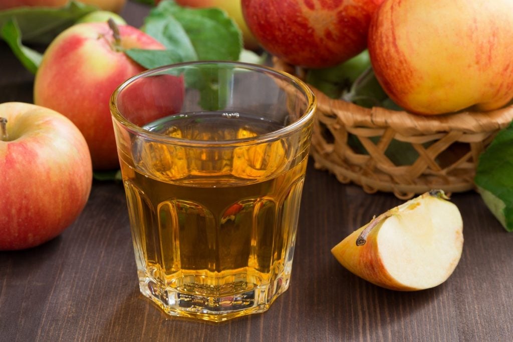 copo de vinagre de maçã ao lado de um pedaço de maçã e de maçãs inteiras