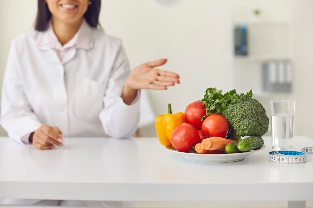 Nutricionista apontando para alimentos saudáveis e copo de água, que são elementos para Dieta e Emagrecer rápido