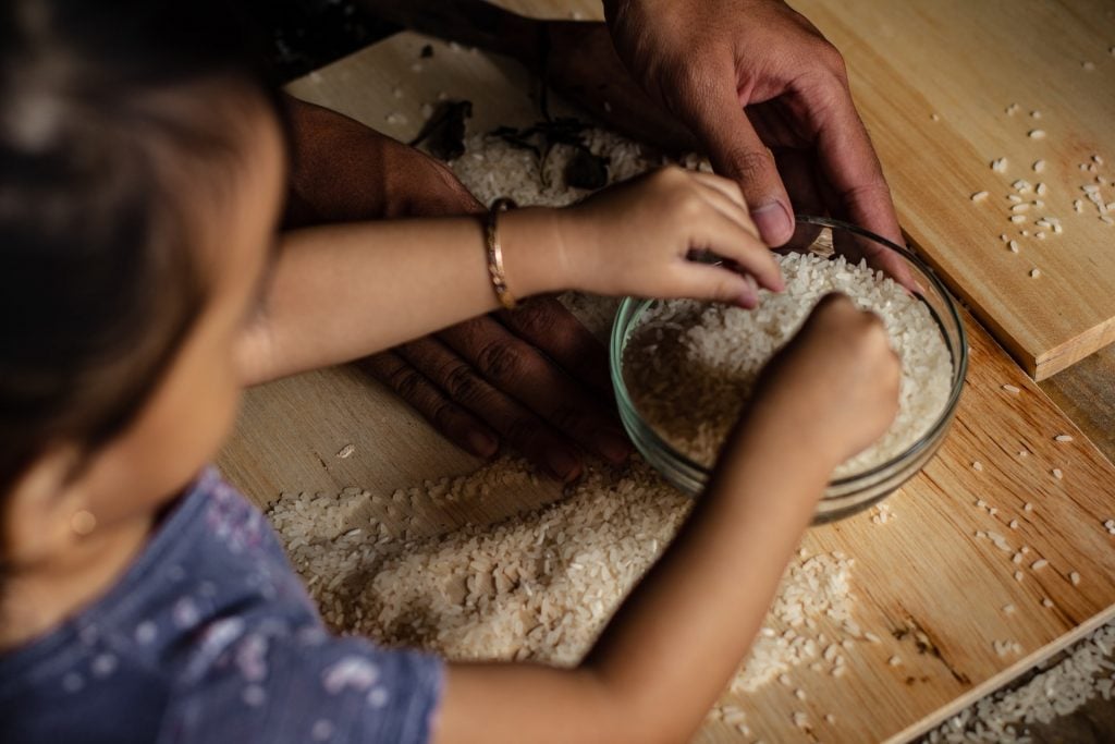 Criança e adulto mexendo em arroz cru, preparando-se para receita de bolinho de arroz simples