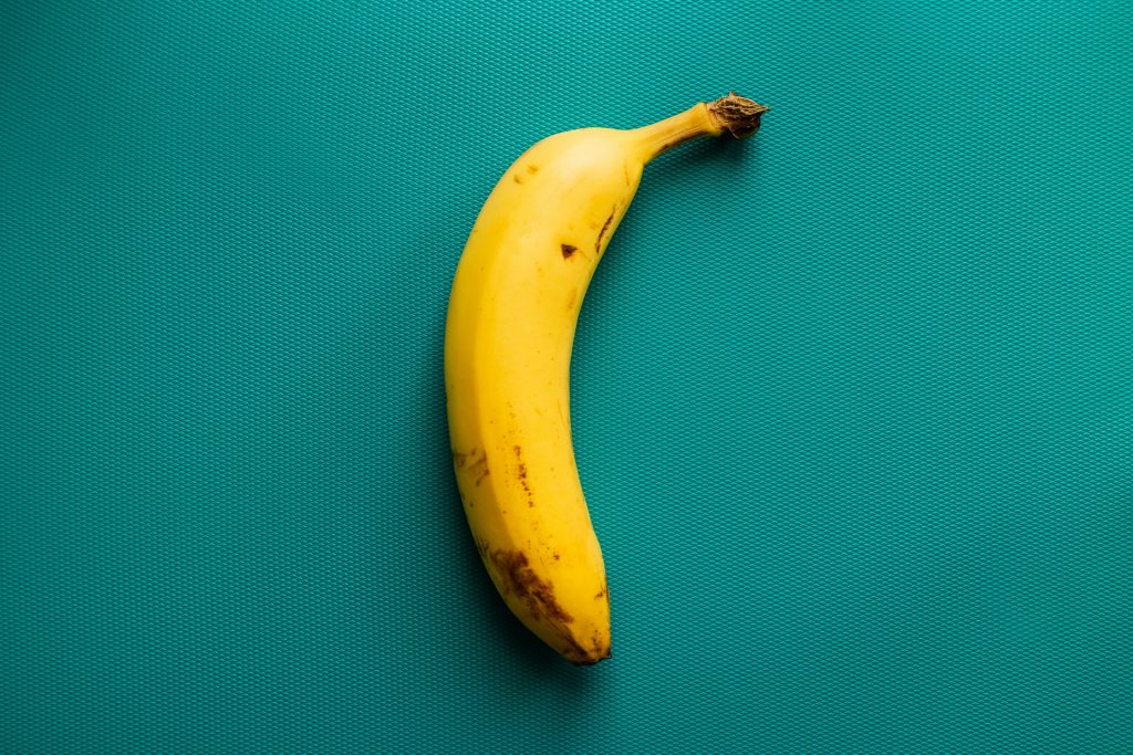 Banana (com fundo verde-água), que é o ingrediente principal dessa receita simples de bolo!