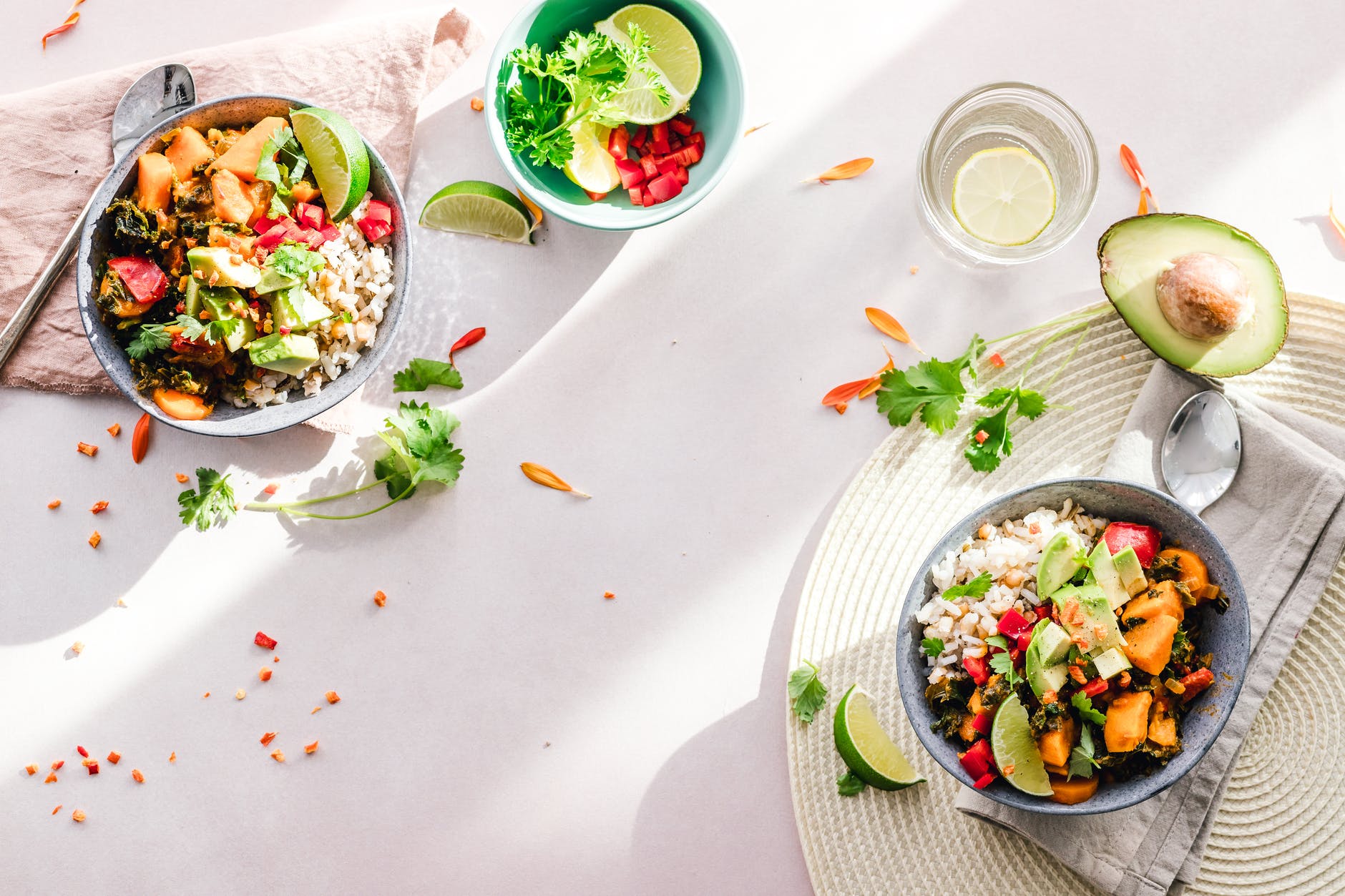 Tigelas com legumes, arroz e vegetais em mesa posta; copo com limão vista de cima