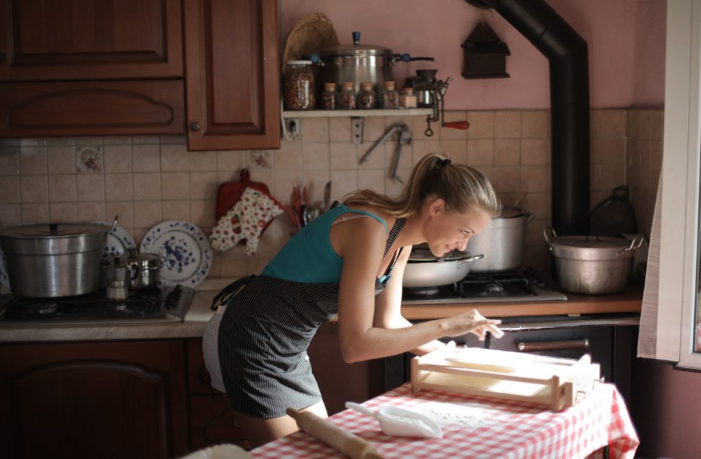 Mulher cozinhando de avental em casa, usando as técnicas do Curso Domine sua Cozinha