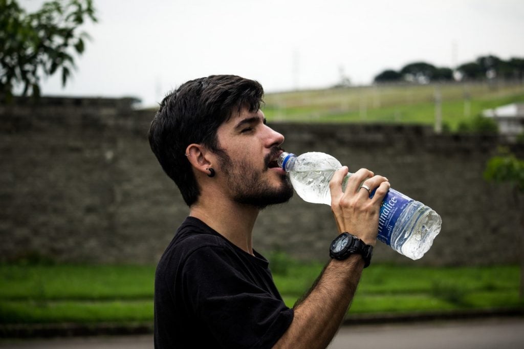 homem bebendo água na garrafa plástica 
