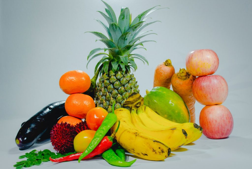foto em fundo cinza com abacaxi, banana, maçã e outras frutas cítricas