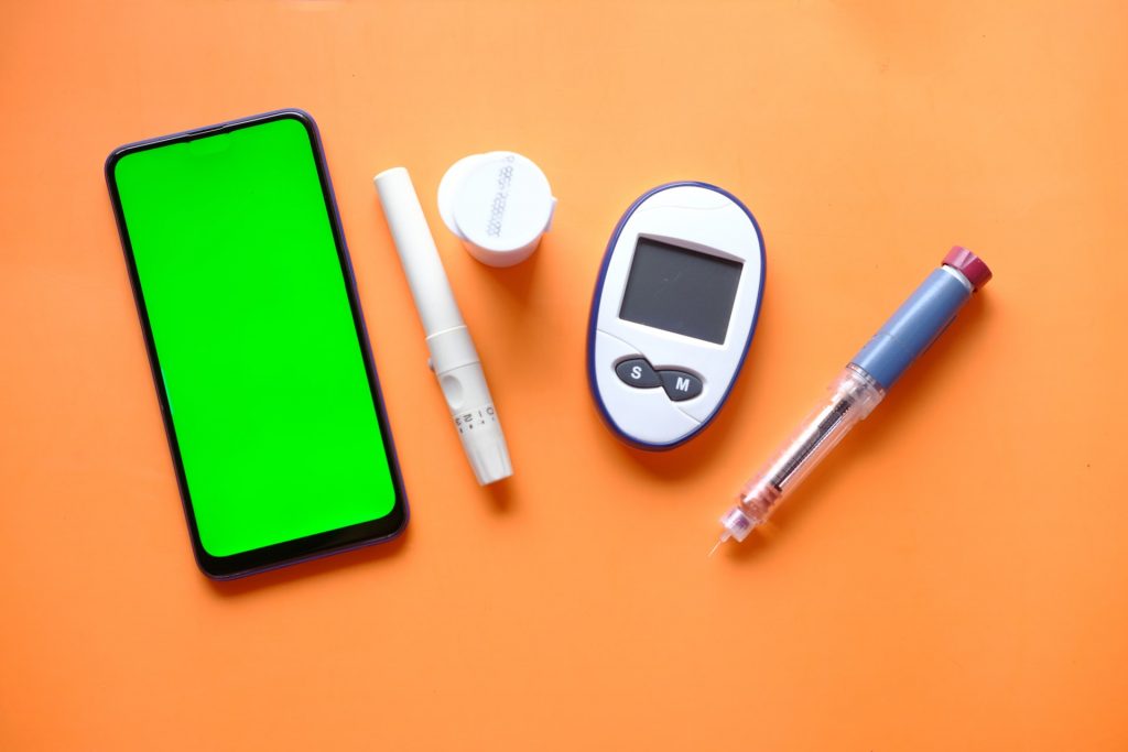 Aparelho para diabetes medidor de glicose, e celular com tela verde ao lado, representando como usar e a cor do logotipo do Aplicativo My Sugr