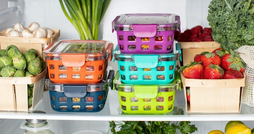 Marmitas de cores variadas na geladeira, com frutas e legumes ao redor