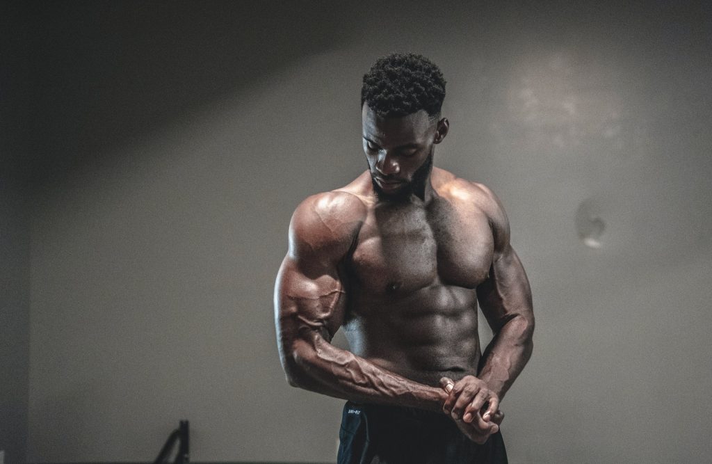 Homem com músculos bem definidos olhando seu próprio bíceps, representando atletas que fazem uso do Growth Suplemento vitamínico