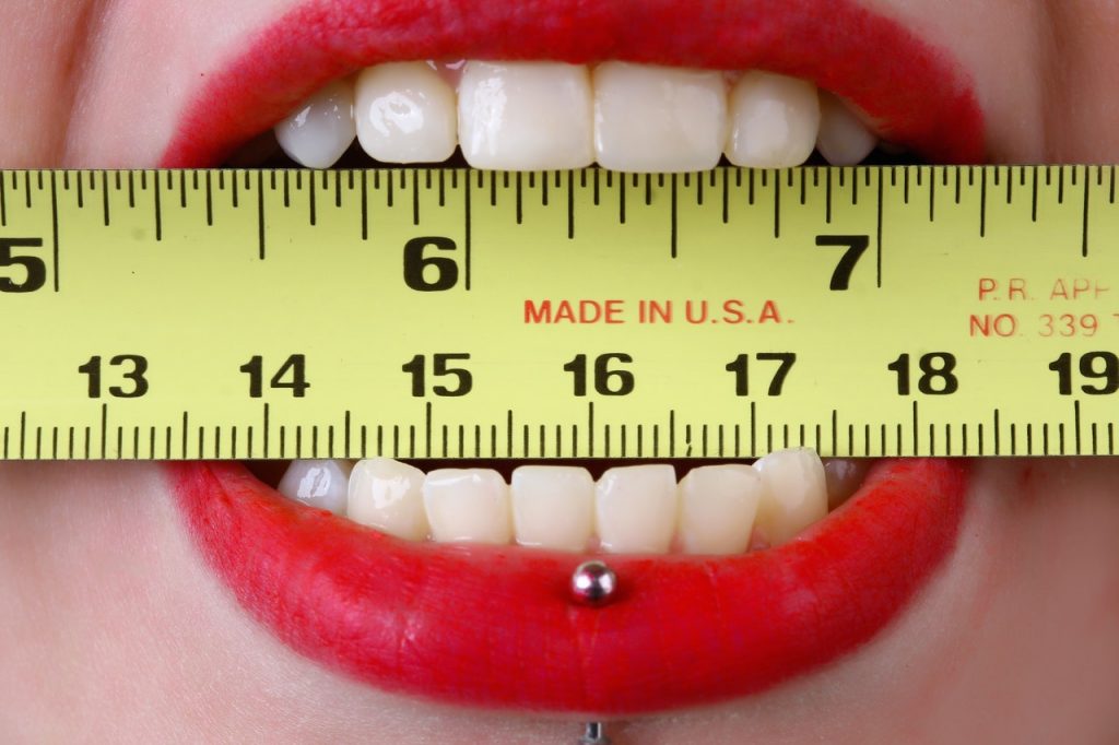 pessoa de batom com fita métrica na boca