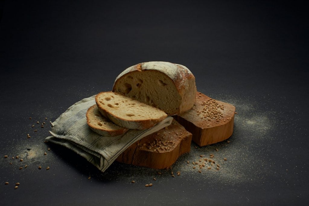 pão caseiro sem ovos cortado em algumas fatias e colocado em cima de tábua de madeira junto com um pano