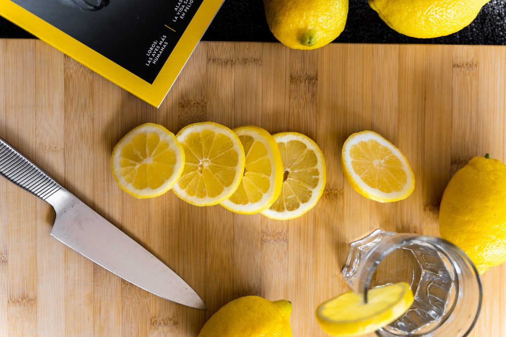 diversas fatias de limão dispostas em tábua de madeira e próximas a uma faca e um copo com água