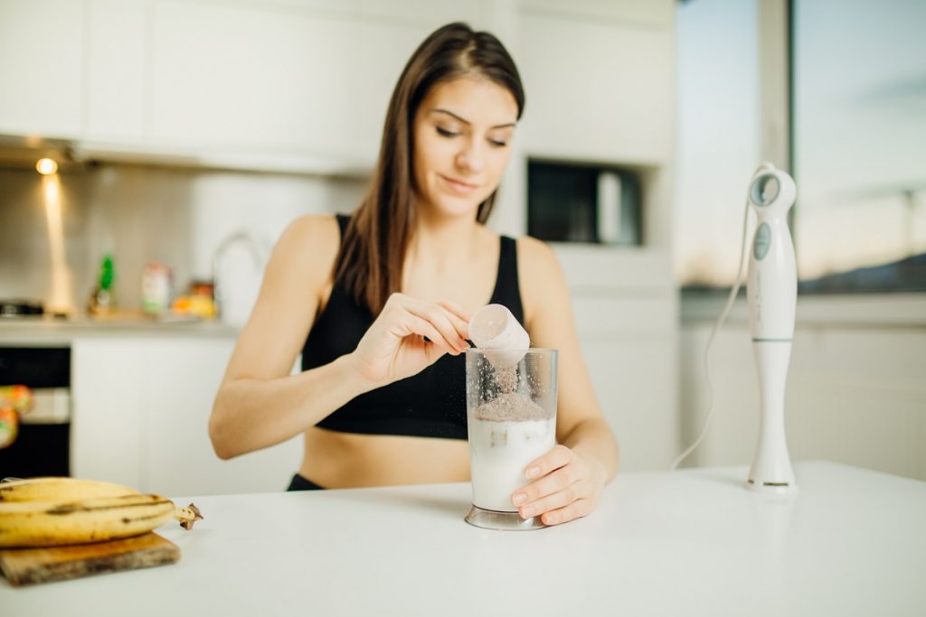 mulher colocando whey protein no copo de leite para tomar um shake