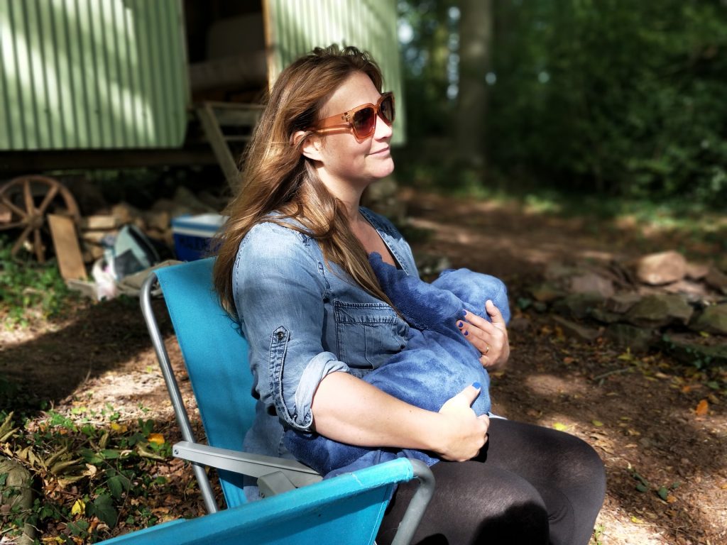 Mãe com óculos escuros amamentando bebê sentada em cadeira em ambiente externo natural sutilmente ensolarado. Simbolizando como emagrecer amamentando