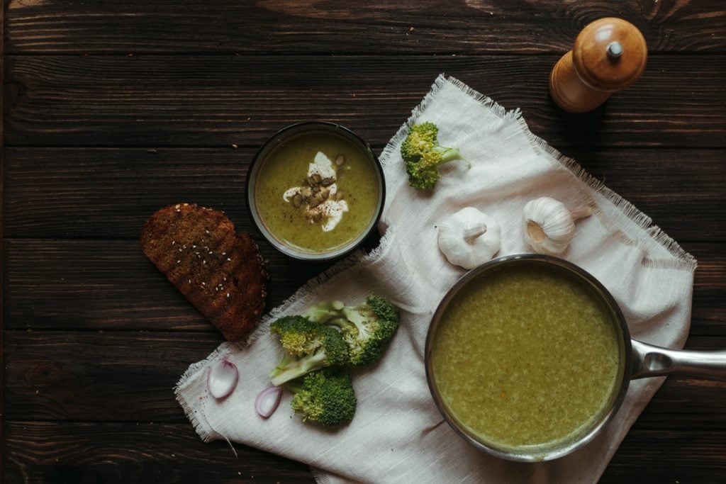pano branco com panela cheia de sopa zero carboidrato em cima; ao lado, brócolis, alho e outros ingredientes do preparo