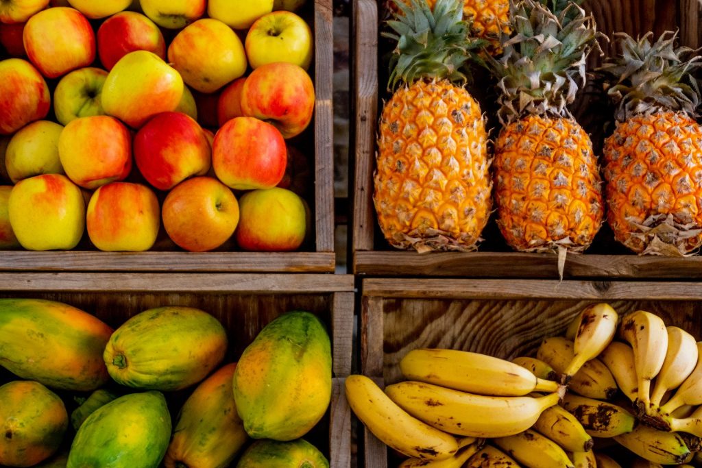 Caixotes abertos com maçãs, abacaxis, mamões e bananas. Maçã, abacaxi e mamão são opções de fruta para emagrecer