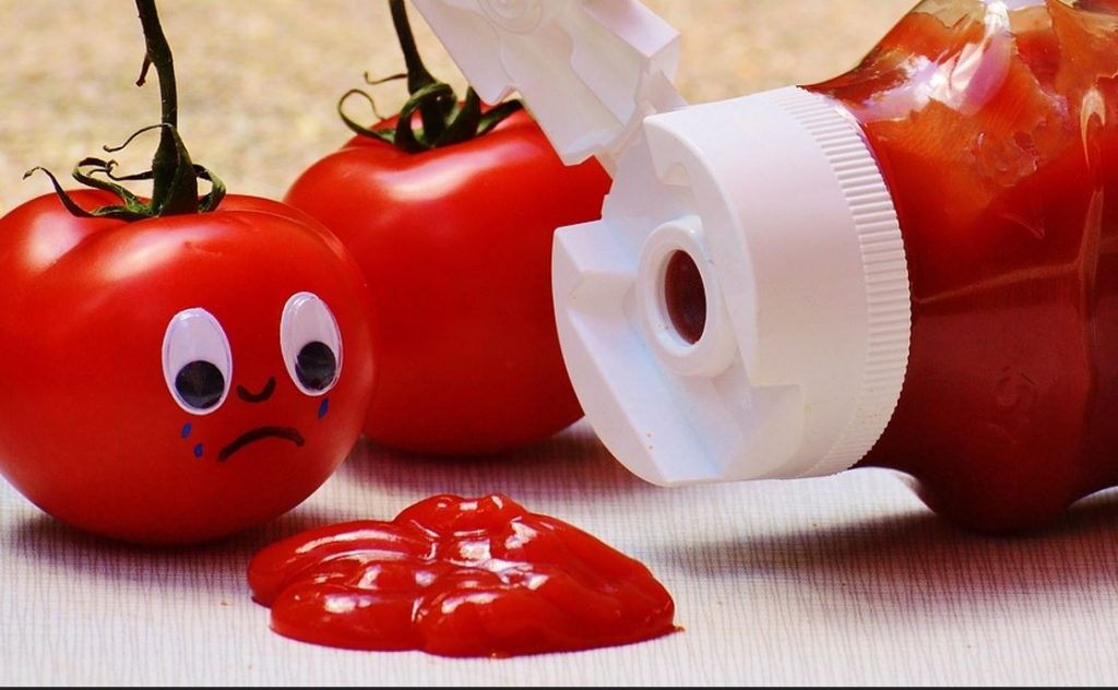 Pote de ketchup virado com tomate com cara chorando