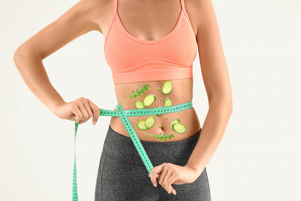 Mulher segurando fita métrica em volta da cintura com imagens de legumes sobre a barriga