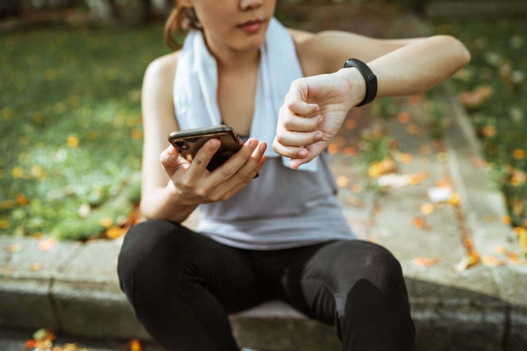 Menina sentada medindo o pulso com celular e smartwatch