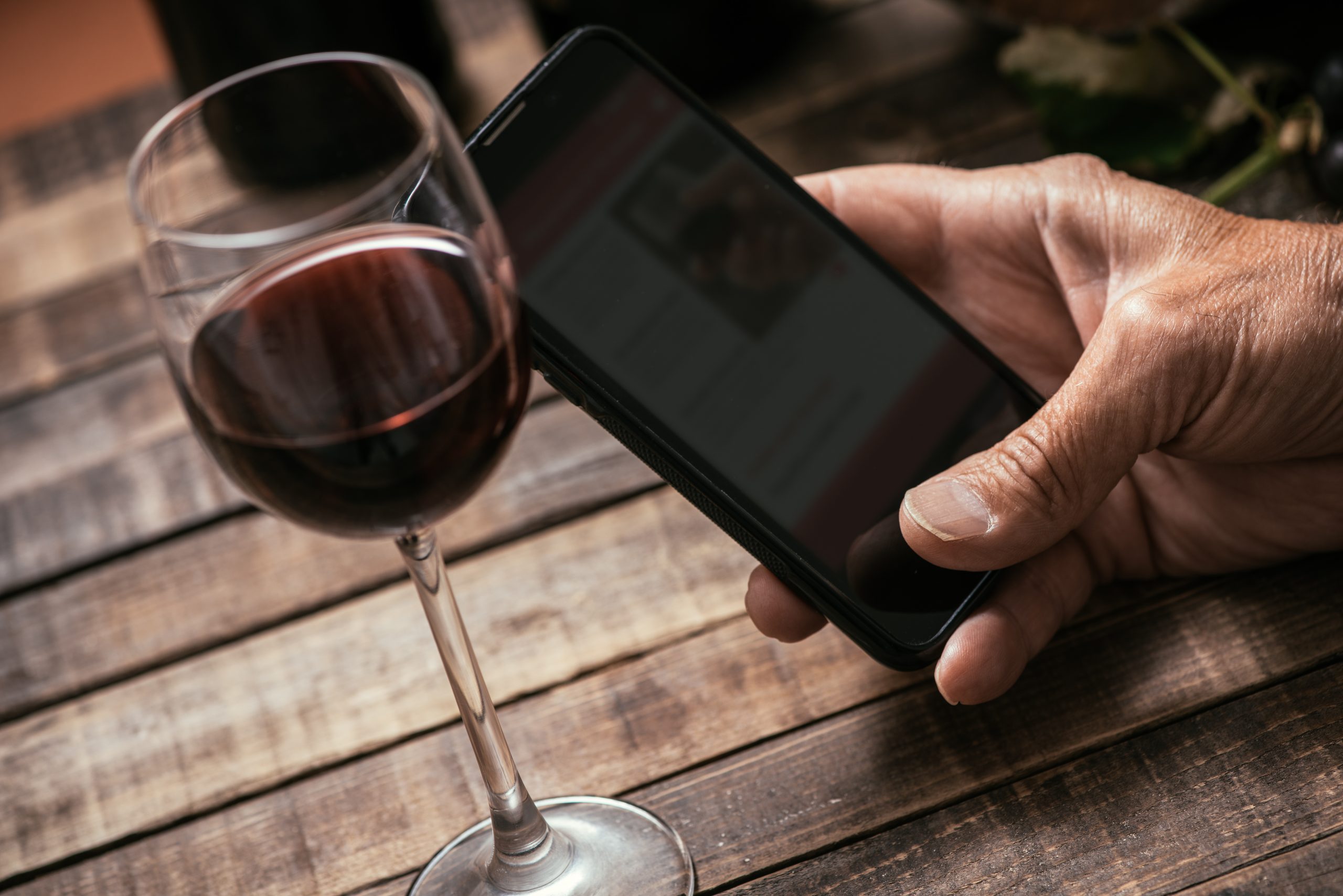 Taça de vinho e mão usando celular