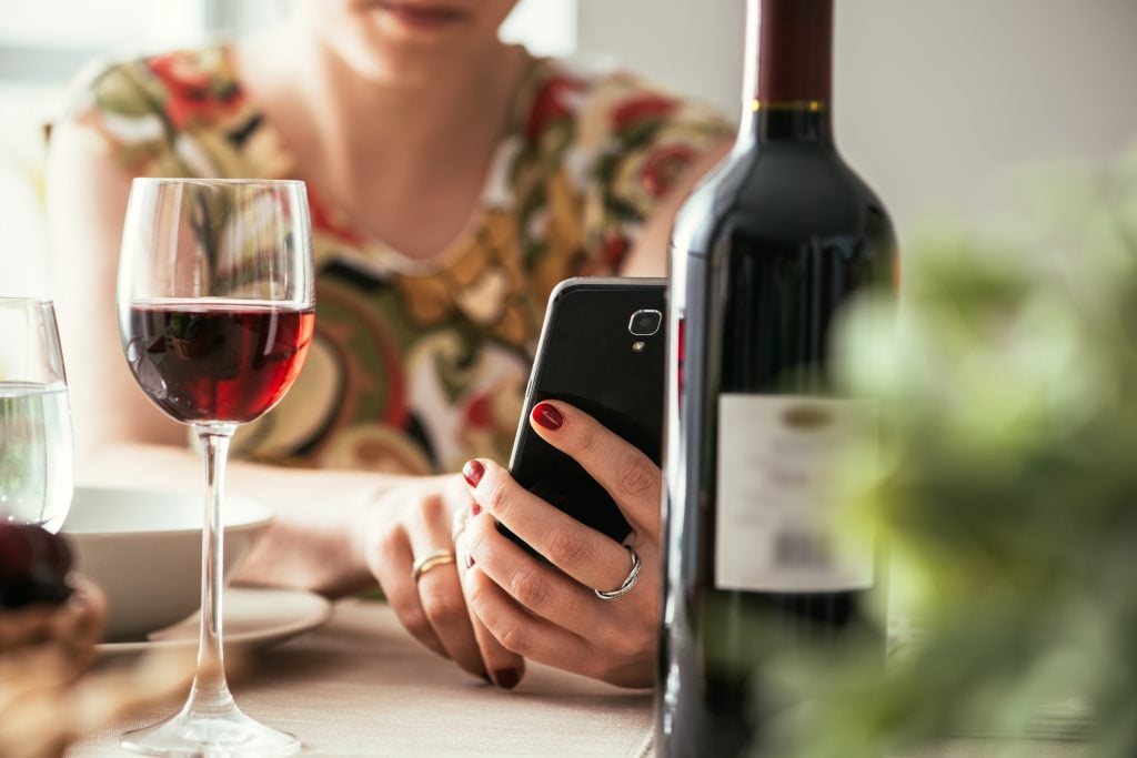 Mulher usando celular com garrafa de vinho