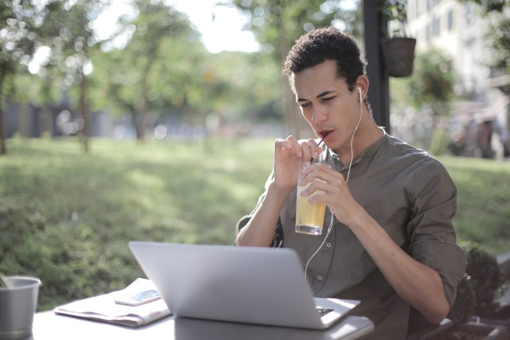 homem de fone de ouvido mexendo no computador e tomando suco de limão
