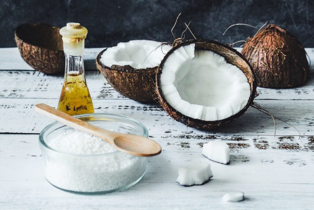 óleo de coco em pote transparente; ao fundo, um coco seco cortado ao meio