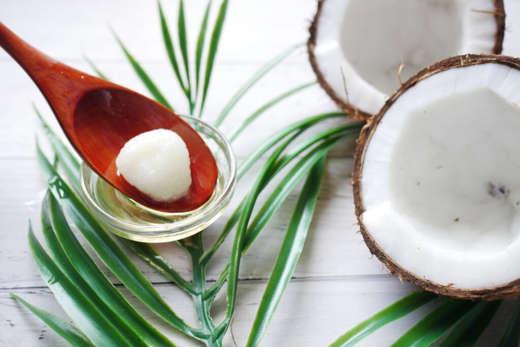 Óleo de coco em pote de vidro ao lado de um coco seco aberto ao meio