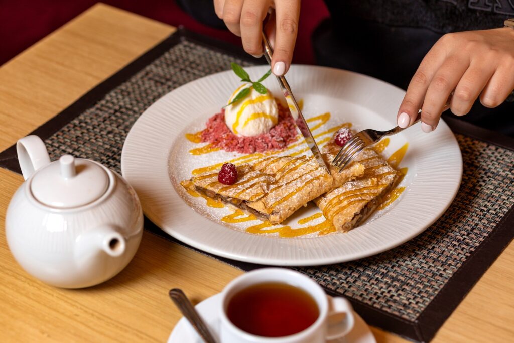 pessoa comendo crepe com bola de sorvete e xícara de chá