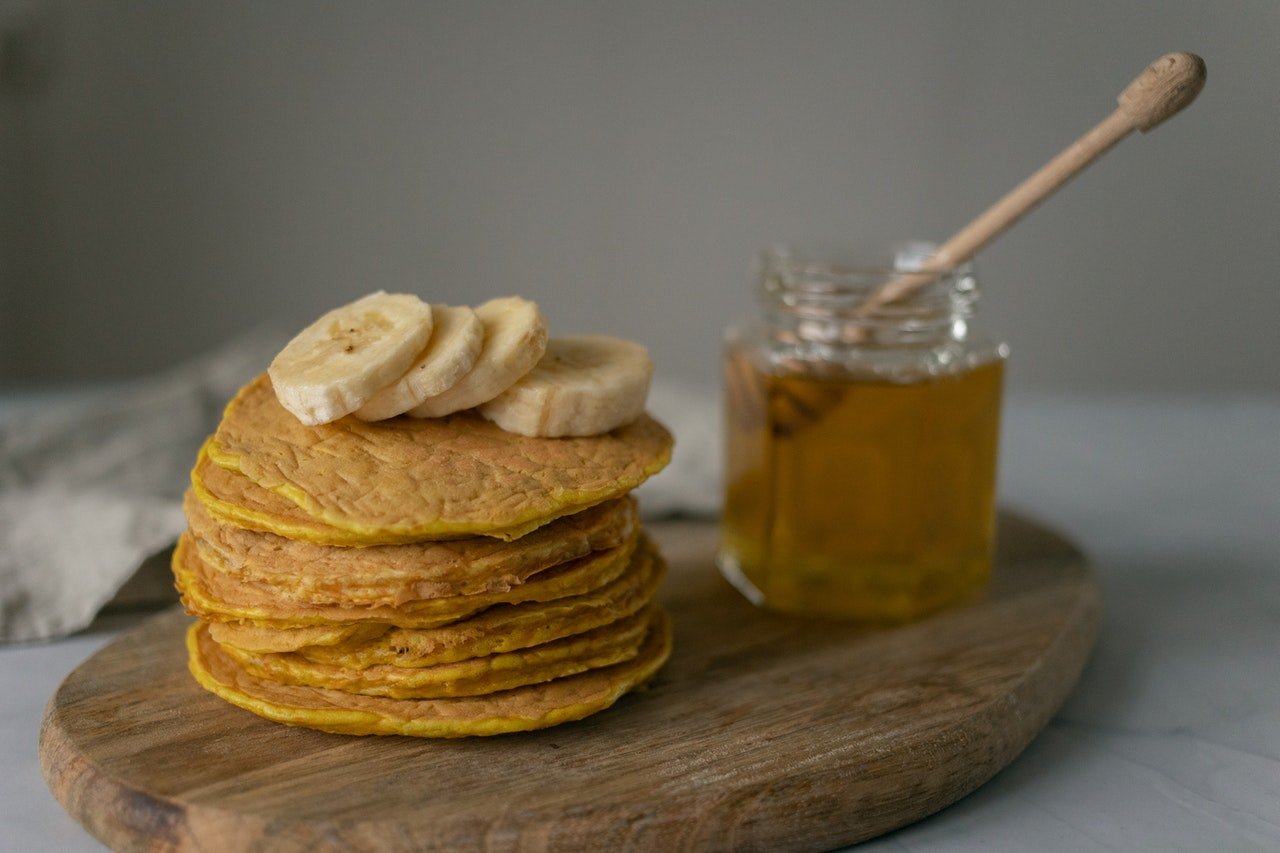 Panquecas empilhadas com rodelas de banana e pote de mel