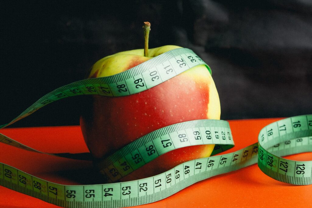 Maçã, que é uma boa fruta num cardápio para emagrecer barato, envolta de uma fita métrica