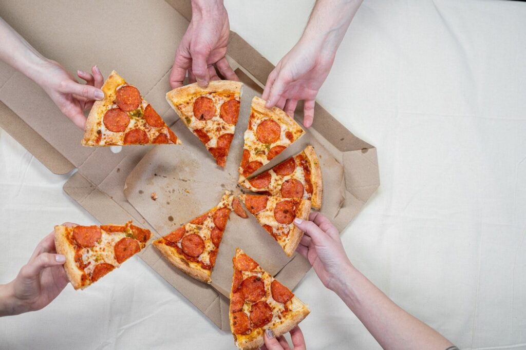 Várias pessoas pegando fatias de pizza da caixa