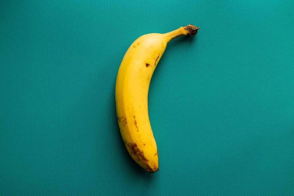 Banana (com fundo verde-água), que é o ingrediente principal dessa receita simples de bolo!