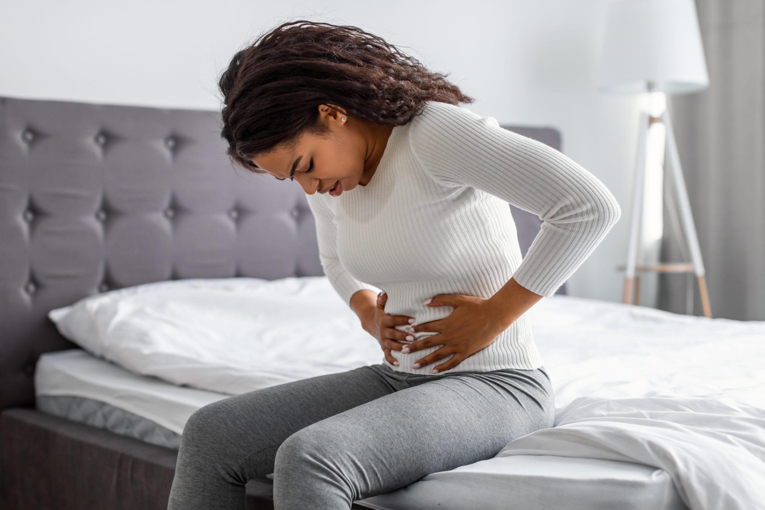 Mulher com dor de estômago sentada em cama com mão na barriga