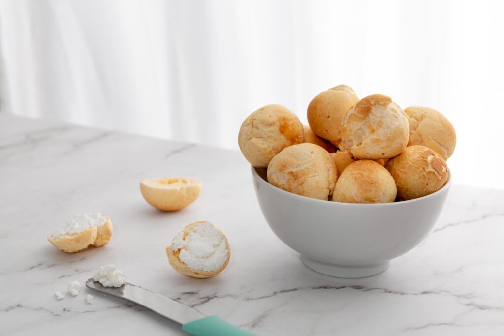 Pães de queijo em recipiente com faca e requeijão