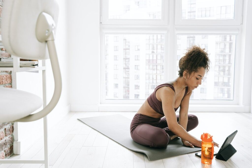 mulher sentada em tapete de ginástica assistindo Programa Mulheres Fit no tablet