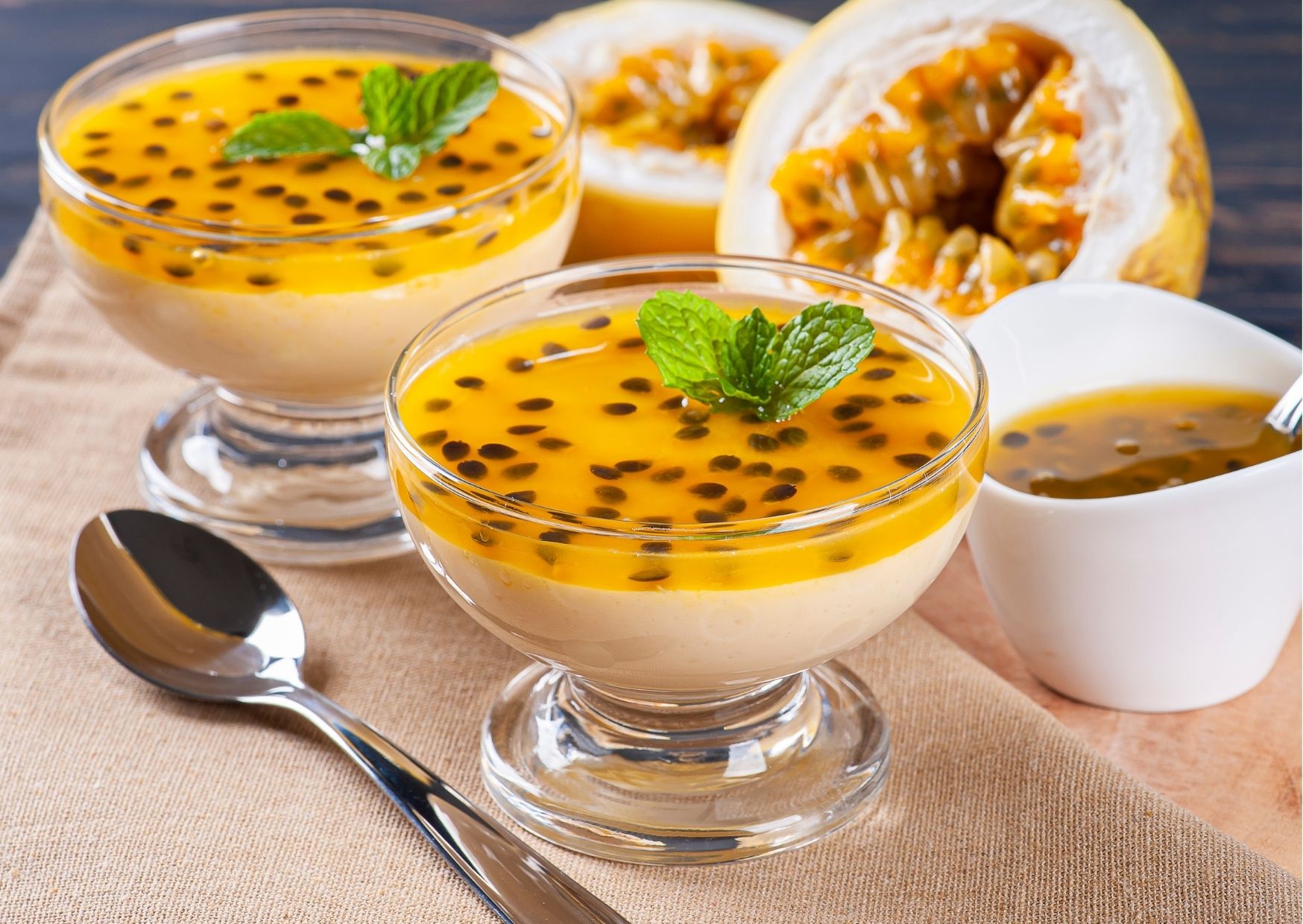 Potes de mousse de maracujá com folhas de hortelã e maracujás ao fundo