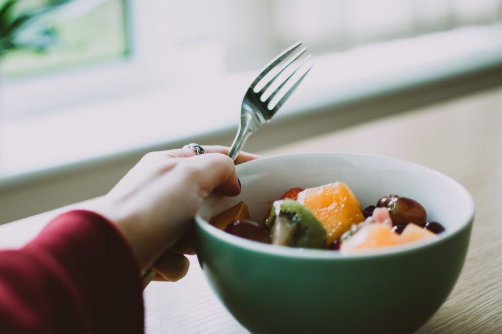 Pessoa com tigela com frutas e garfo
