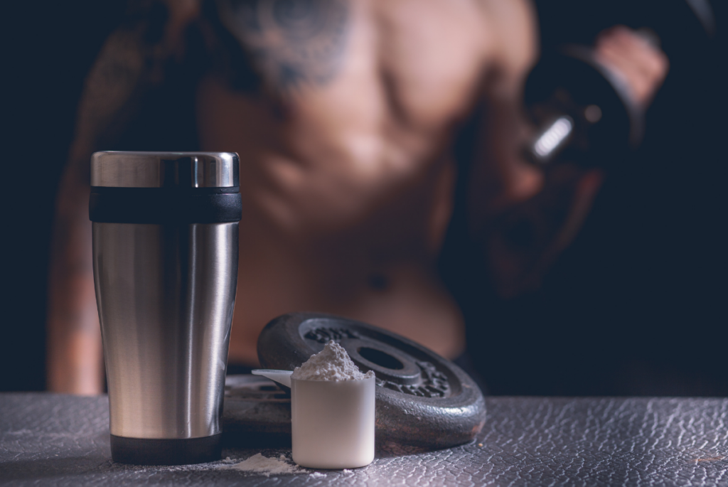 Halter, copo e scoop de whey com homem ao fundo