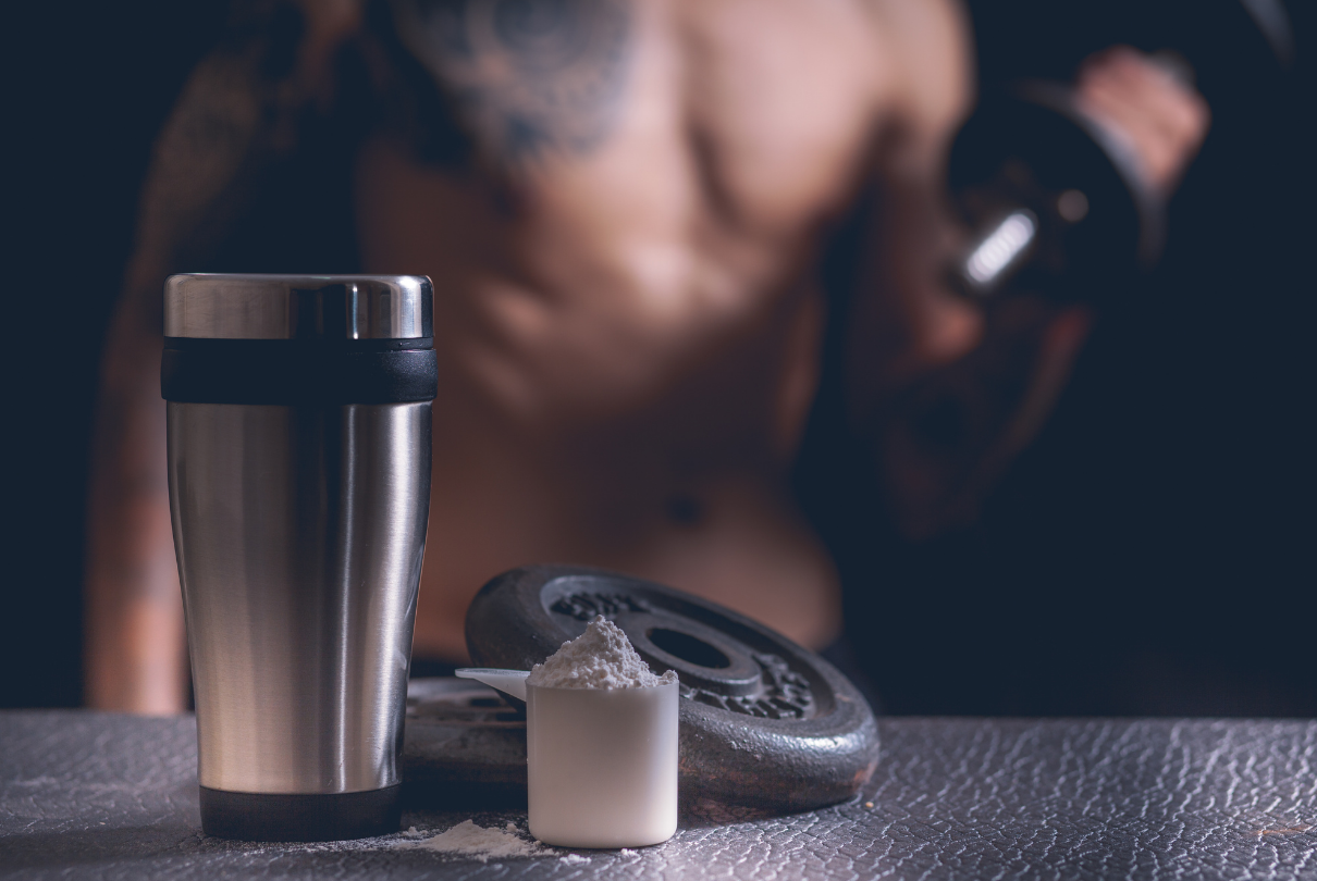 Halter, copo e scoop de whey com homem ao fundo