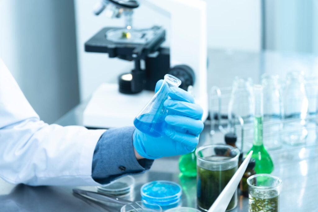 Cientista em laboratório com recipientes e microscópio