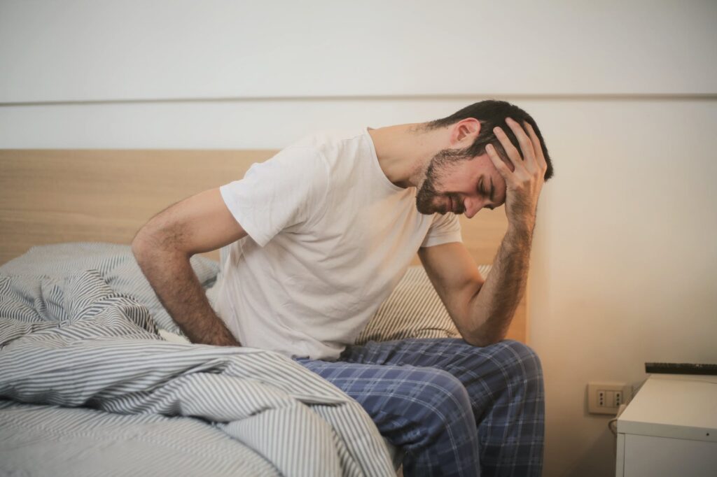 Pessoa sentada na cama com dor de cabeça