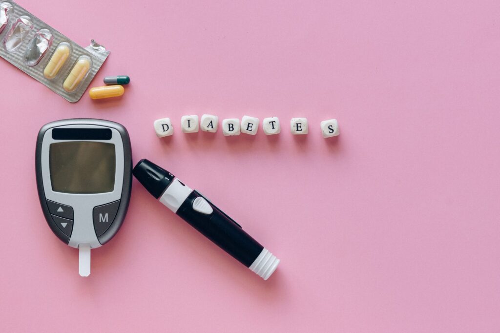 Medidor de glicose, pílulas, letras formando a palavra diabetes em fundo rosa