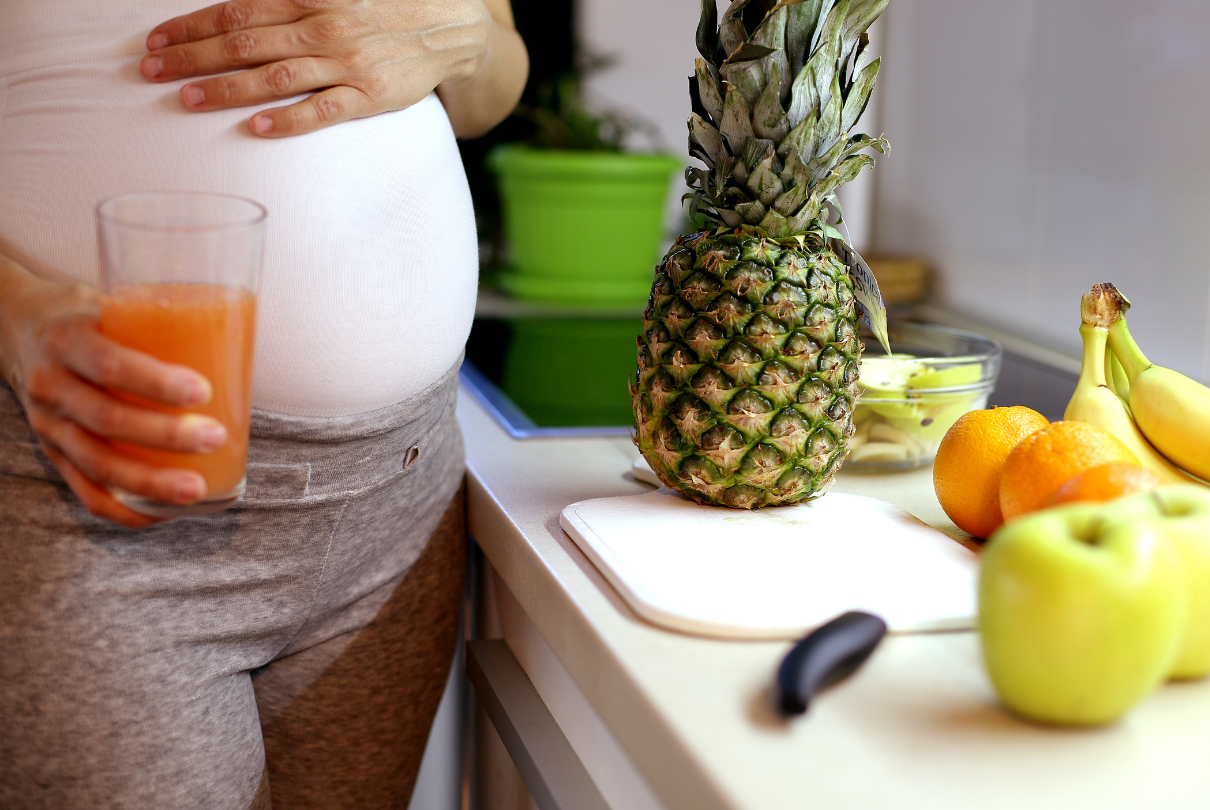 grávida com suco na mão e frutas do lado