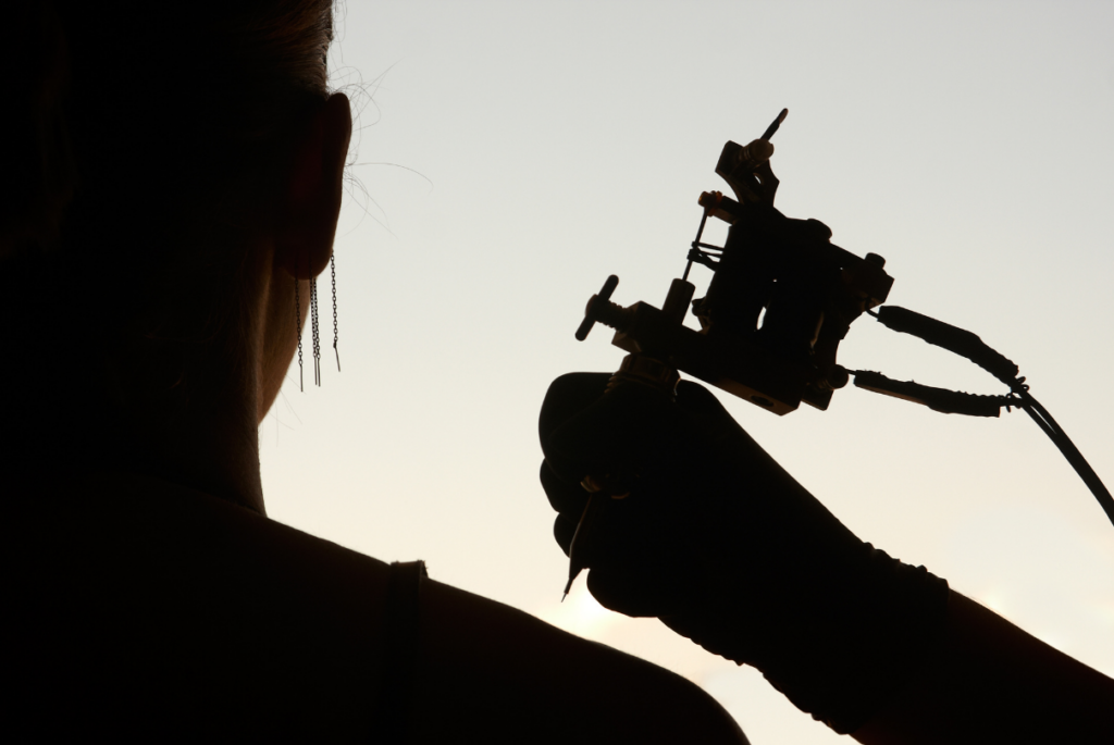 mulher com máquina de tatuagem ao lado
