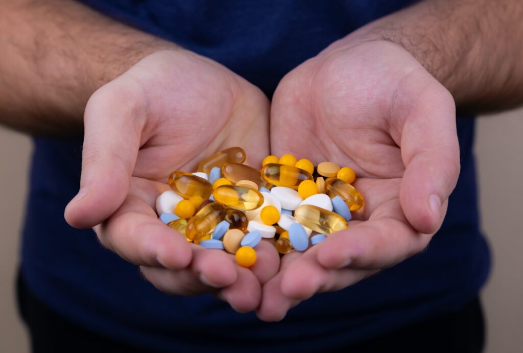 Duas mãos masculinas segurando pílulas, cápsulas de vitaminas manipuladas, suplementos vitamínicos, complexo vitamínicos, cápsulas gelatinosas etc