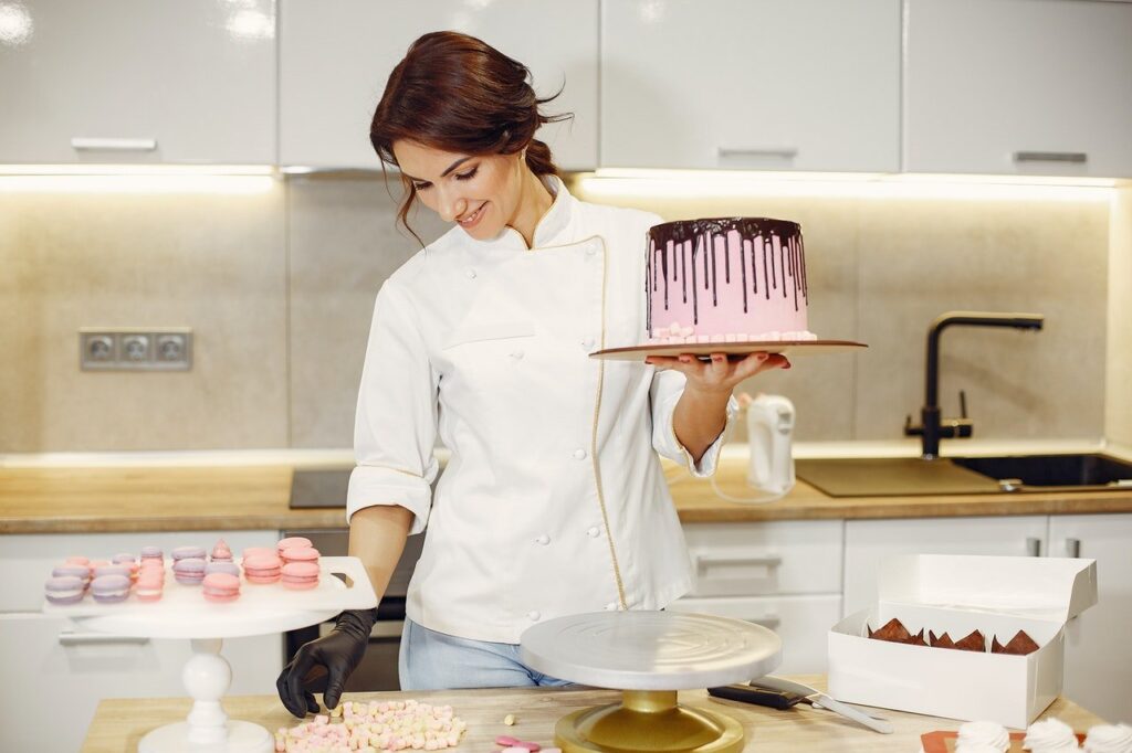Mulher segurando bolo profissional, com cobertura. Confeitos como macaroons sobre a mesa.