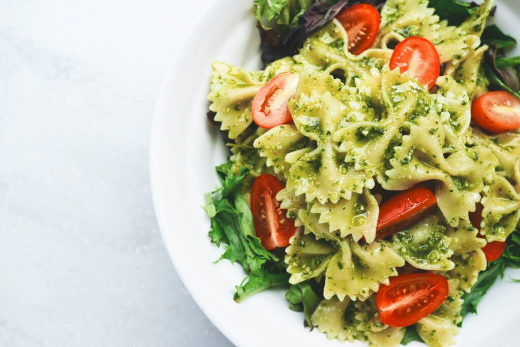 Prato com macarrão Farfalle (também conhecido como gravatinha ou borboleta) com folhas, tomates cortados e tempero. Massas são um exemplo da diversidade abordada nas opções de Cursos online de Gastronomia Learncafe 
