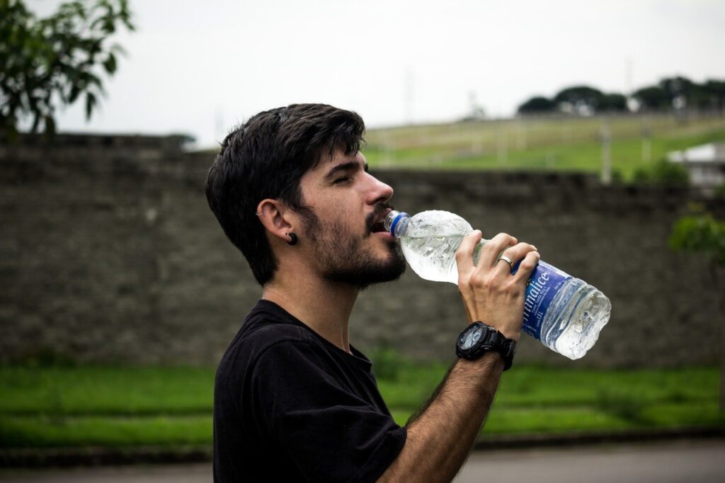 homem bebendo água na garrafa plástica