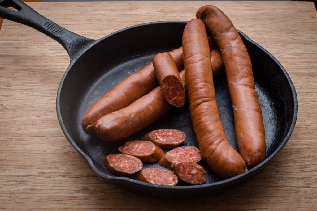 embutidos inteiros e fatiados em uma frigideira