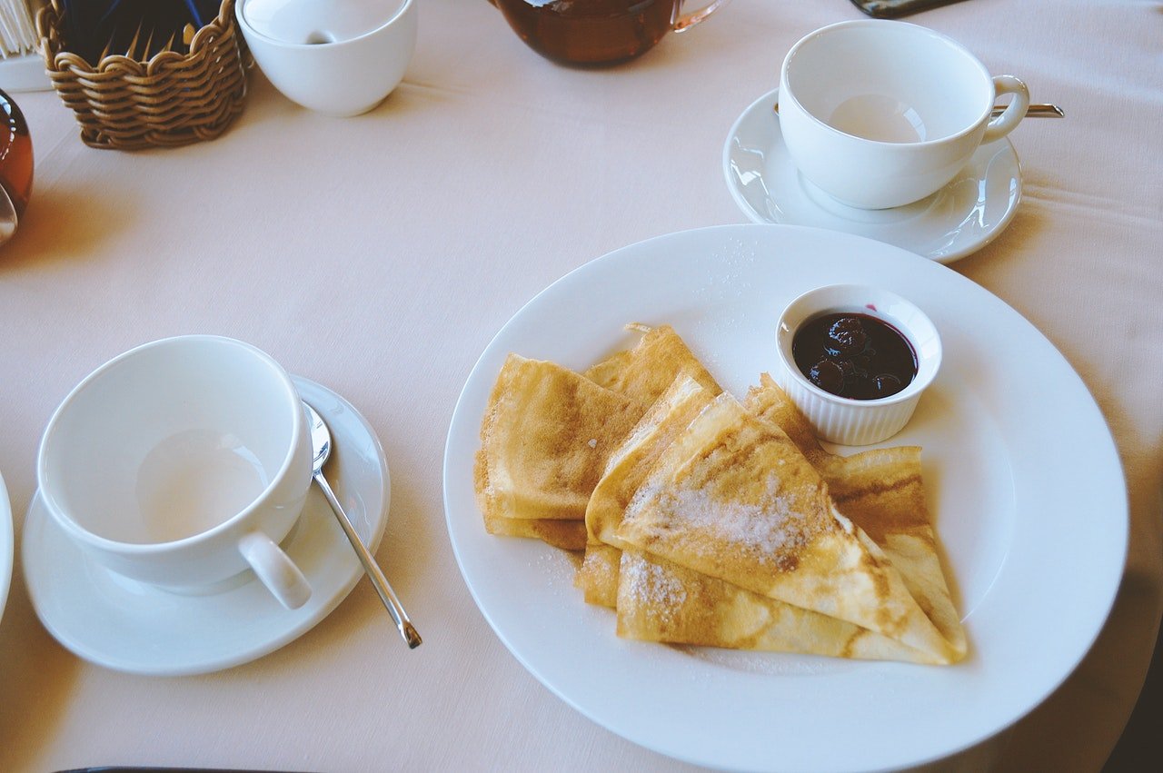 mesa com xícara e prato de crepe com geléia