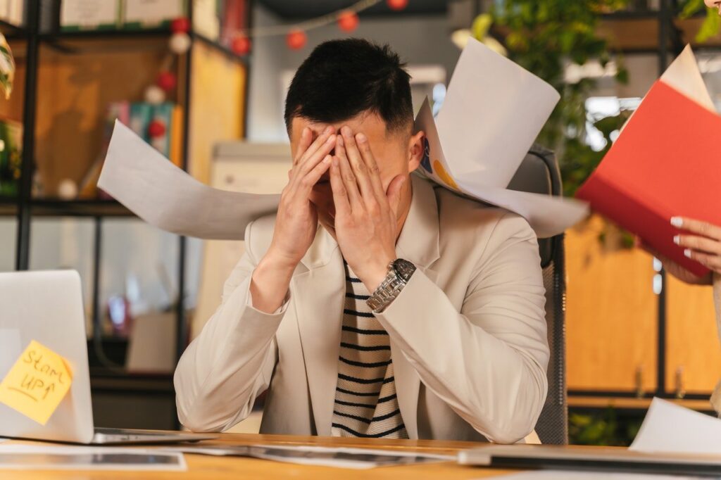 homem sentado na mesa de trabalho, em frente ao notebook, muito cansado e cheio de trabalho
